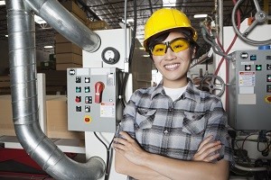 Portrait of female industrial worker smiling while standing in factory with machines in background