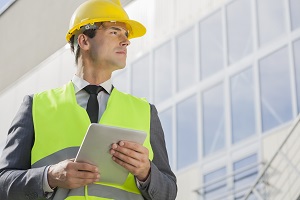 Young male architect with digital tablet looking away outside building
